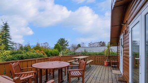 A wooden deck with a table and chairs, a glass door, and a view of a garden.