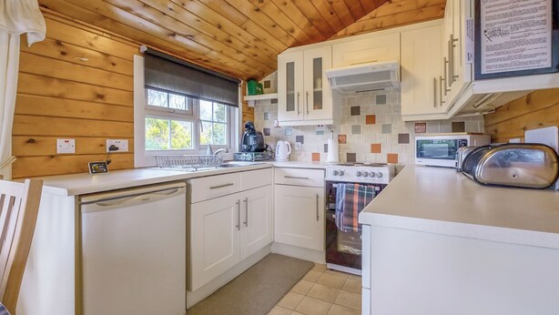 A compact kitchen with wooden walls, a stove, a microwave, and a dishwasher.