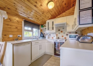 A compact kitchen with wooden walls, a stove, a microwave, and a dishwasher.