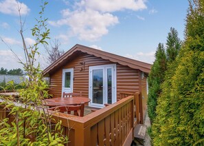 A log cabin with a deck, a table, and chairs.