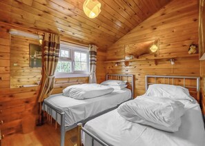 Et værelse i en træhytte med to metal senge, et vindue med gardiner og en hængende lampe.