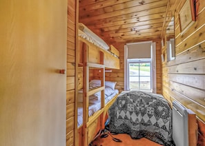 A wooden cabin room with bunk beds, a window, and a door.