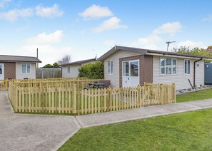 A row of mobile homes with a wooden fence in front, a picnic table, and a small shed.