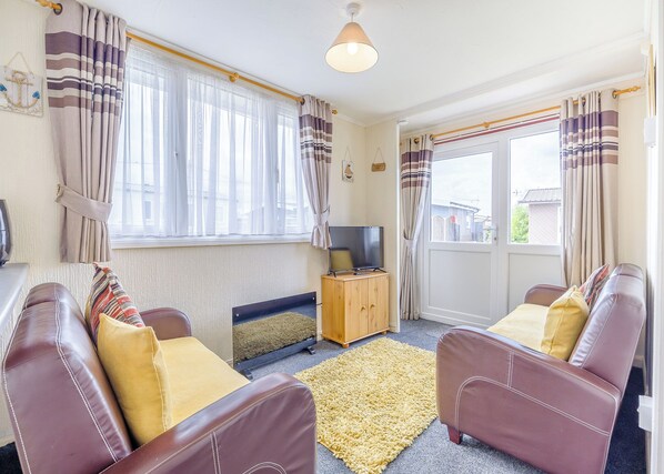 A living room with two leather sofas, a television on a wooden cabinet, and a large window with curtains.