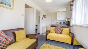 A compact living space with a sofa, armchair, and a small kitchen area. - 1 bedroom accommodation in Anderby Creek, Mablethorpe (Anderby Creek, Mablethorpe)