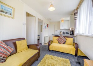 A compact living space with a sofa, armchair, and a small kitchen area.