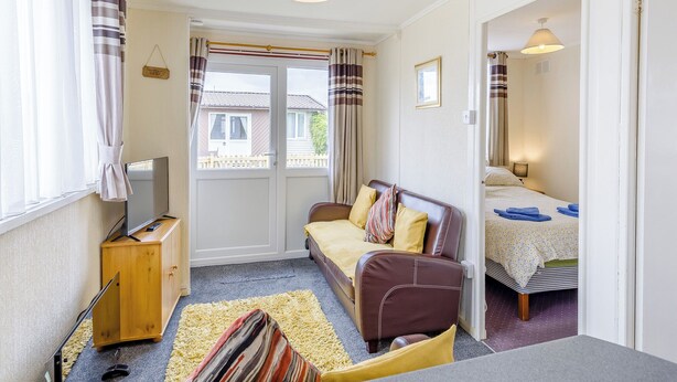A cozy room with a sofa, a TV, a wooden cabinet, and a bed with a patterned bedspread. - 1 bedroom accommodation in Anderby Creek, Mablethorpe (Anderby Creek, Mablethorpe)