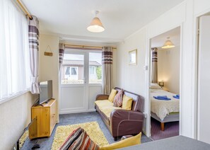 A cozy room with a sofa, a TV, a wooden cabinet, and a bed with a patterned bedspread.