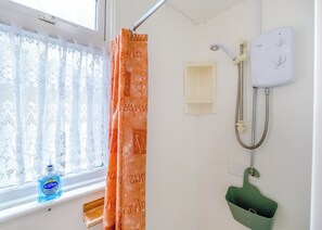 A bathroom with a window, a shower, a green sink, and a bottle of liquid soap.