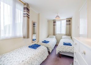 Una habitación de hotel con dos camas individuales, un espejo, un aparador y una ventana con cortinas.