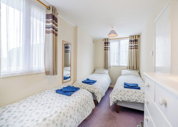 Una habitación de hotel con dos camas individuales, un espejo, un aparador y una ventana con cortinas.