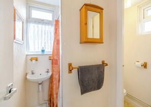 Un baño con lavamanos, ventana, espejo, toallero y soporte para papel higiénico.
