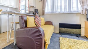 A compact living space with a kitchenette, a sofa with cushions, a small table, and a window with curtains. - 1 bedroom accommodation in Anderby Creek, Mablethorpe (Anderby Creek, Mablethorpe)