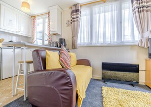 A compact living space with a kitchenette, a sofa with cushions, a small table, and a window with curtains.