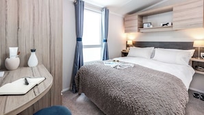 A hotel room with a bed, bedside tables, a desk with a chair, a window with curtains, and a shelf with items. - 2 bedroom accommodation in Cresswell beach (Cresswell beach)