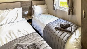 A bedroom with two beds, a window with curtains, and a wooden headboard. - 1 bedroom accommodation in Tunstall, Nr Hull (Tunstall, Nr Hull)