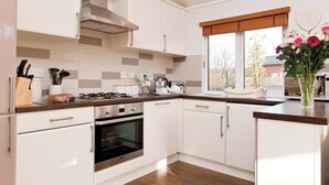 A modern kitchen with white cabinets, a stainless steel range, and an oven. There is a window with a view of the outside, and a vase with flowers on the counter. - 1 bedroom accommodation in Narberth, Nr Tenby (Narberth, Nr Tenby)
