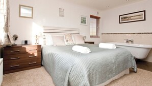 A bedroom with a bed, a dresser, a vanity, and a bathtub. - 1 bedroom accommodation in Narberth, Nr Tenby (Narberth, Nr Tenby)