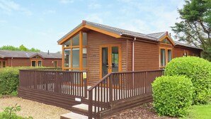 A wooden cabin with a balcony, surrounded by greenery and a gravel path. - 1 bedroom accommodation in Narberth, Nr Tenby (Narberth, Nr Tenby)