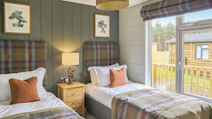 A room with two beds, a nightstand with a lamp, and a window with a view of a wooden structure outside. - 3 bedroom accommodation in Lauder (Lauder)