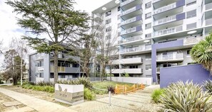 Een modern appartementencomplex met meerdere balkons, een hekwerk en een aangelegde tuin met bomen en struiken.