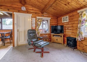 A wooden cabin interior with a leather chair, a television, a small table, and a fireplace.
