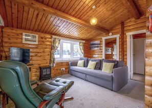 A log cabin interior with a sofa, leather chair, television, and a fireplace.