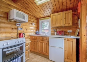 A wooden cabin kitchen with a stove, microwave, refrigerator, wooden cabinets, and a window.