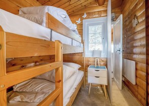 Eine Holzhütte mit Etagenbetten, einem kleinen Nachttisch, einer Lampe und einem Fenster mit Jalousien.