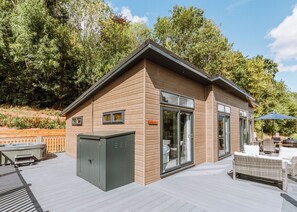 A modern wooden cabin with a deck, a hot tub, and outdoor furniture.