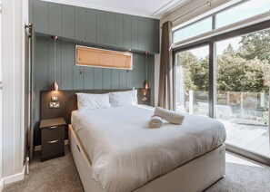 A bedroom with a large bed, bedside tables, a wall-mounted light, and a view through a large window.