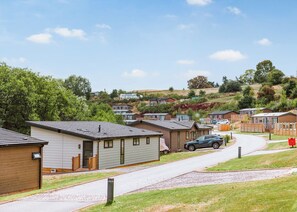 A row of mobile homes with a paved road in front, surrounded by greenery and hills.