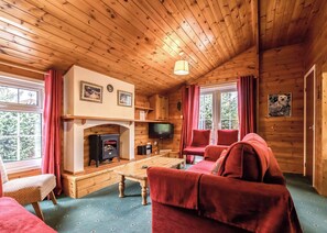 A cozy cabin interior with a fireplace, television, red furniture, and wooden walls.