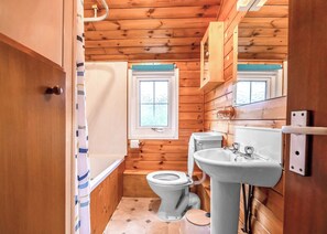 Une petite salle de bain en bois, équipée de toilettes, d’un lavabo et d’une fenêtre.