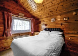 A wooden cabin bedroom with a bed, window, curtains, and a sign indicating a fire exit.