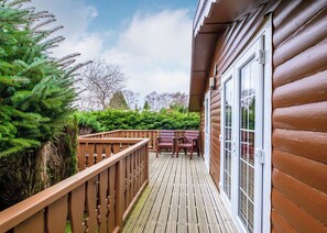 A wooden deck with a railing, a table with chairs, and a glass door.