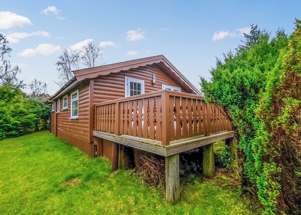 A wooden cabin with a deck, surrounded by lush greenery.
