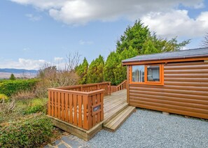 Une cabane dotée d’une terrasse en bois, d’une fenêtre à cadre orange et offrant une vue sur le paysage environnant.
