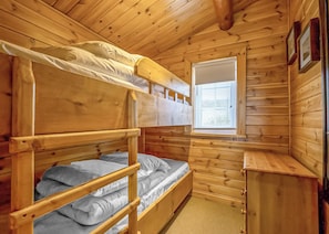 Une chambre dans un chalet en bois, avec des lits superposés, une fenêtre avec des stores et une commode en bois.