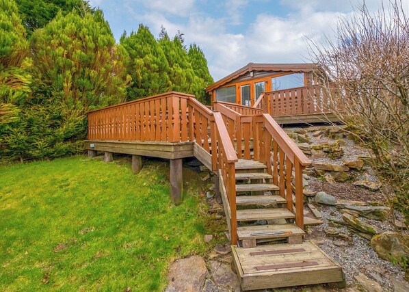 Una terraza de madera con escaleras que conducen a una cabaña con ventanas amplias.