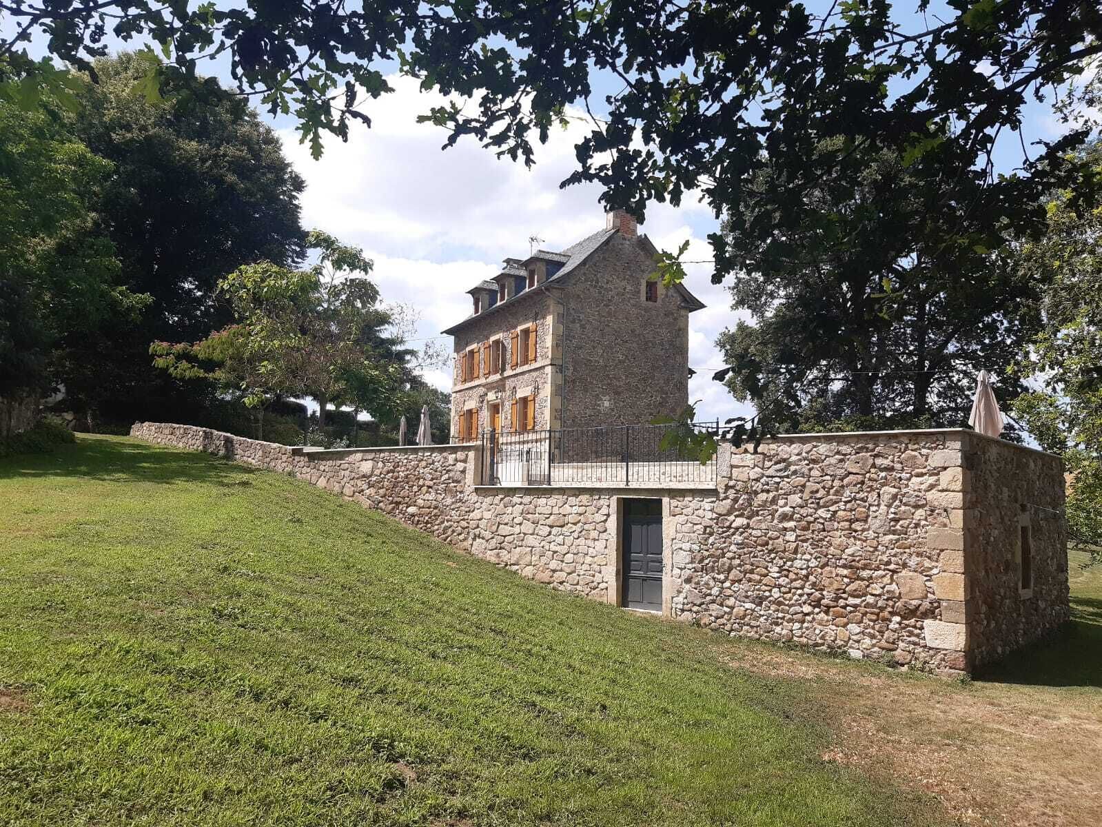 A stone building with a balcony and a door, surrounded by a stone wall and a grassy area.