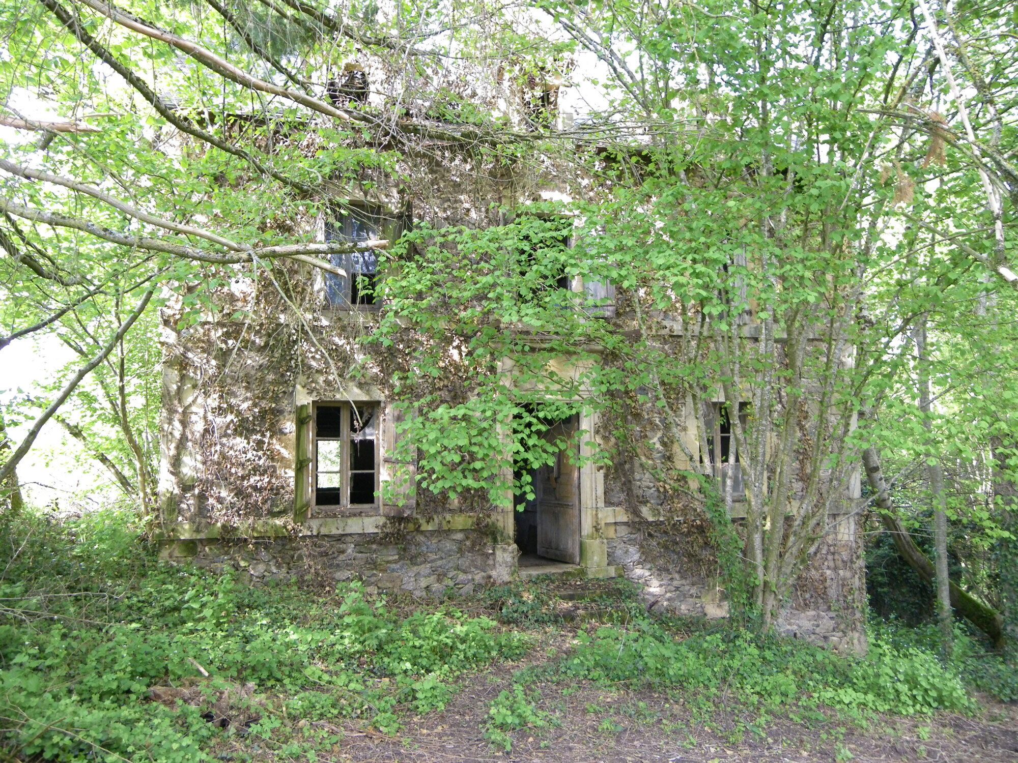 An abandoned stone building overgrown with vegetation, featuring a single visible window and a door.