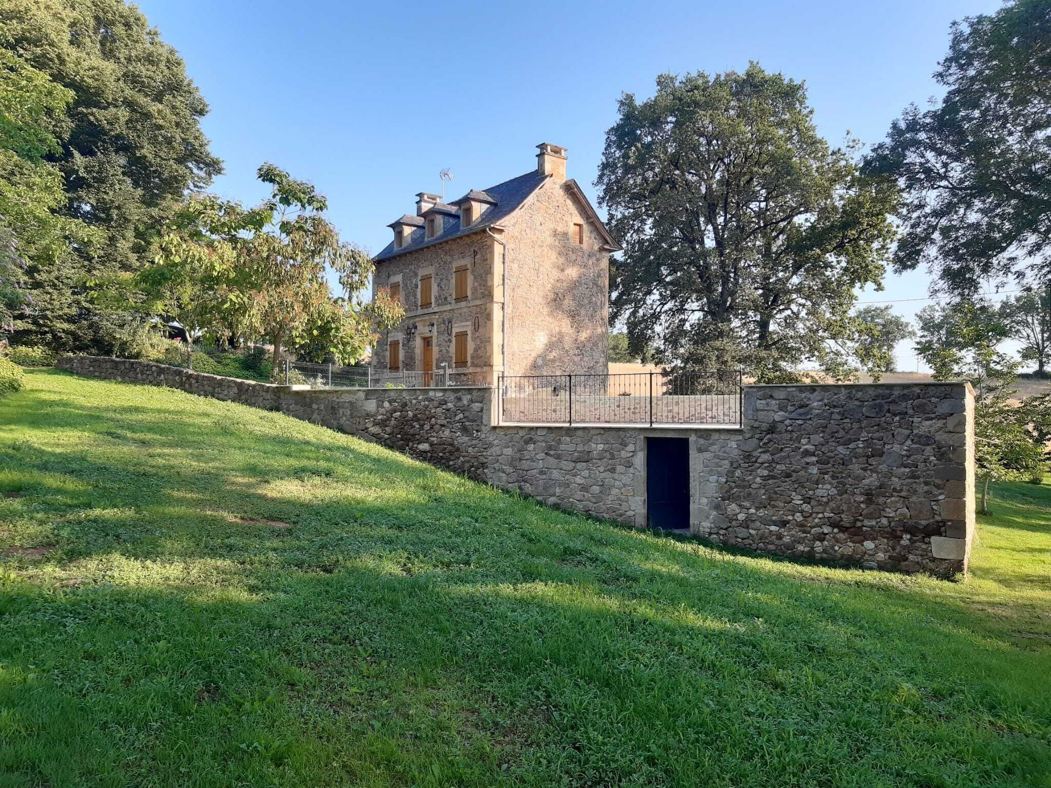 A stone building with a balcony, surrounded by a grassy area and trees.
