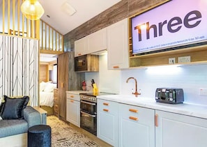A modern kitchen with white cabinets, a built-in oven, a microwave, and a large screen displaying 'Three'.