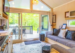 A cozy room with a sofa, a dining table, and chairs, a kitchen area, and a large sliding glass door leading to an outdoor deck.