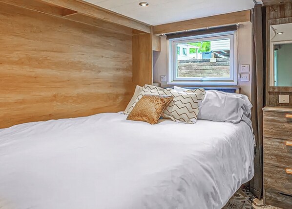 A bedroom with a wooden wall, a bed with white bedding, patterned pillows, a window with a view, and a wooden dresser.