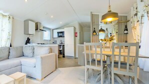 A modern living space with a sofa, a dining table with chairs, a kitchen area, and a visible ceiling light fixture. - 2 bedroom accommodation in Carnforth (Carnforth)