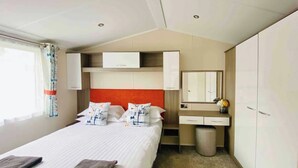 A hotel room with a bed, a bedside table, a mirror, a wardrobe, and a window with curtains. - 2 bedroom accommodation in Carnforth (Carnforth)