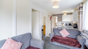 Un espacio habitable compacto con kitchenette, dos sofás grises con cojines, y una puerta visible que da a otra habitación.