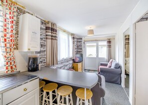 A compact kitchen with a bar stool area, a coffee maker, and a television.